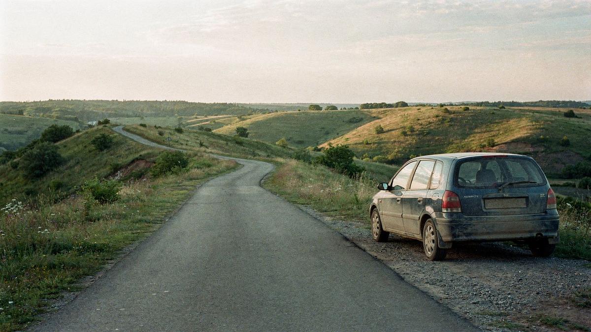 Quiet countryside road outside Kyiv with a compact rental car stopped at a roadside viewpoint